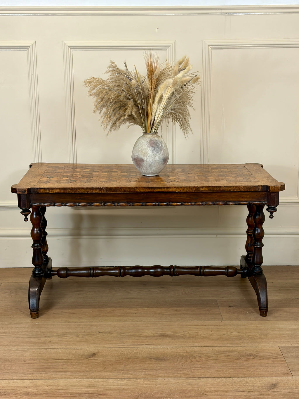 Wooden table with a vase of dried plants against a paneled wall.