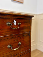 Wooden dresser with brass handles against a neutral wall.