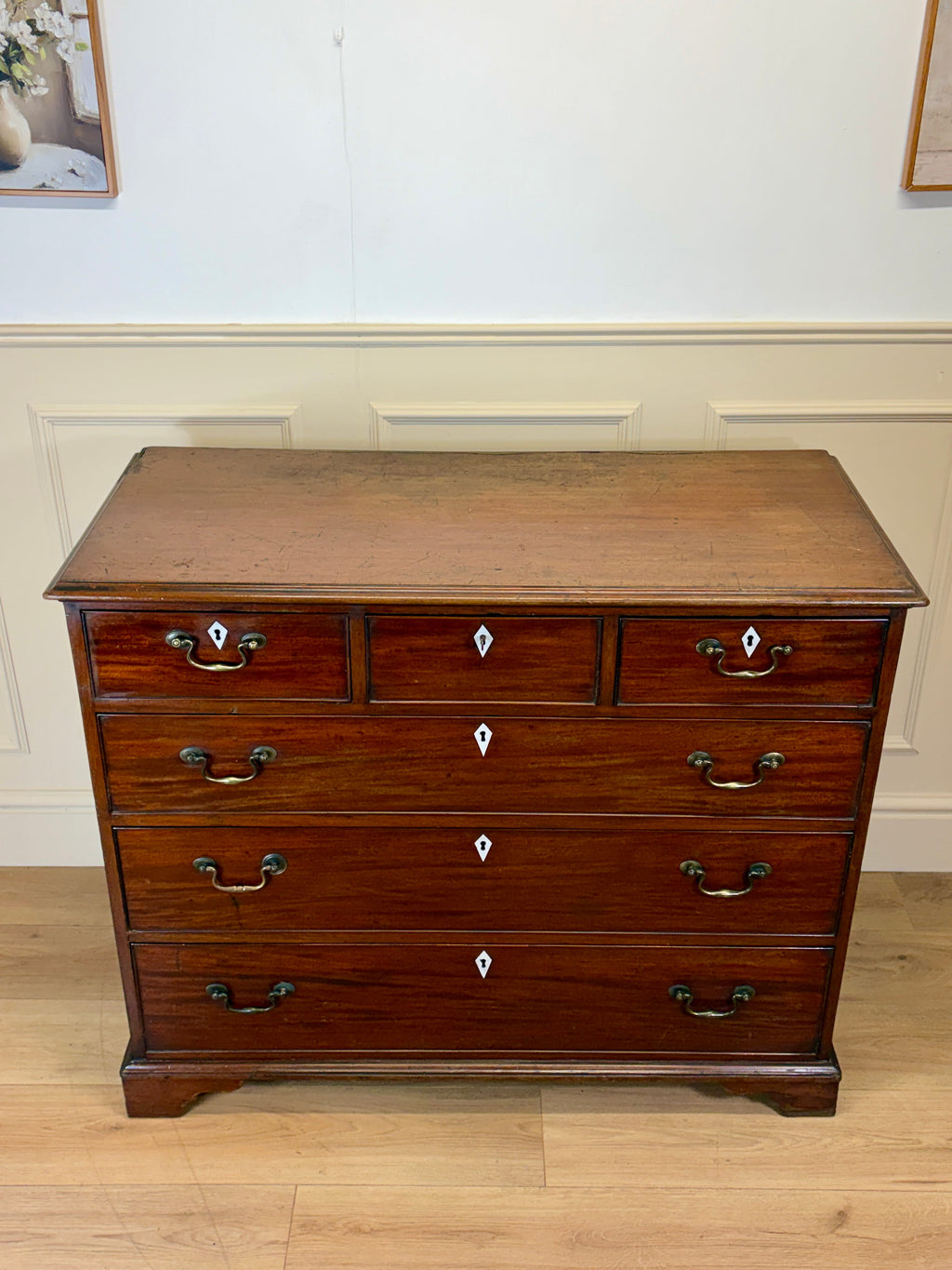 Wooden dresser with multiple drawers on a wooden floor against a white wall.