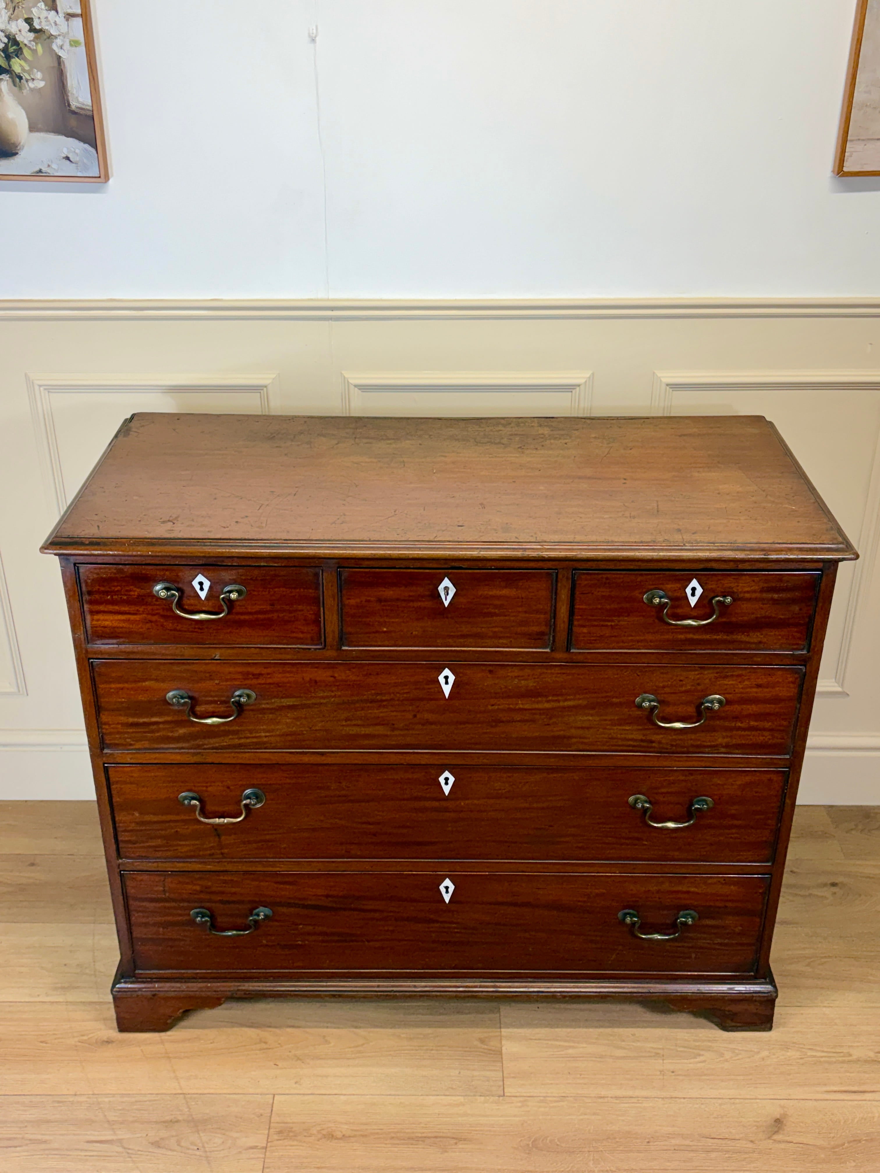 Wooden dresser with multiple drawers on a wooden floor against a white wall.