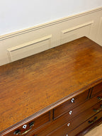 Wooden dresser with multiple drawers against a white wall.