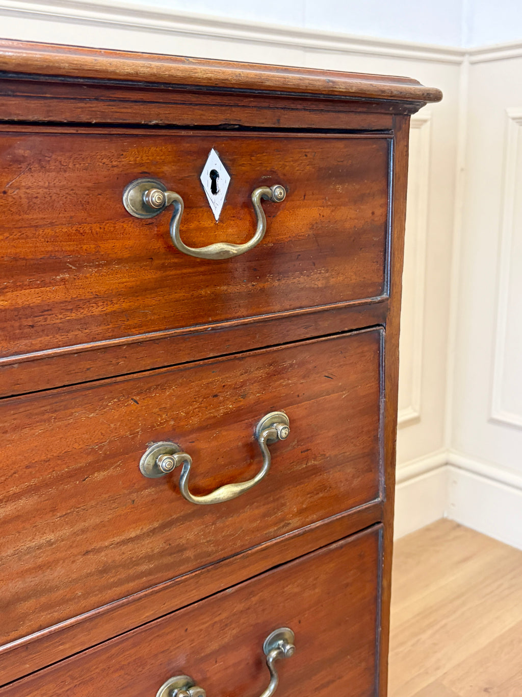 Wooden dresser with brass handles against a white wall.