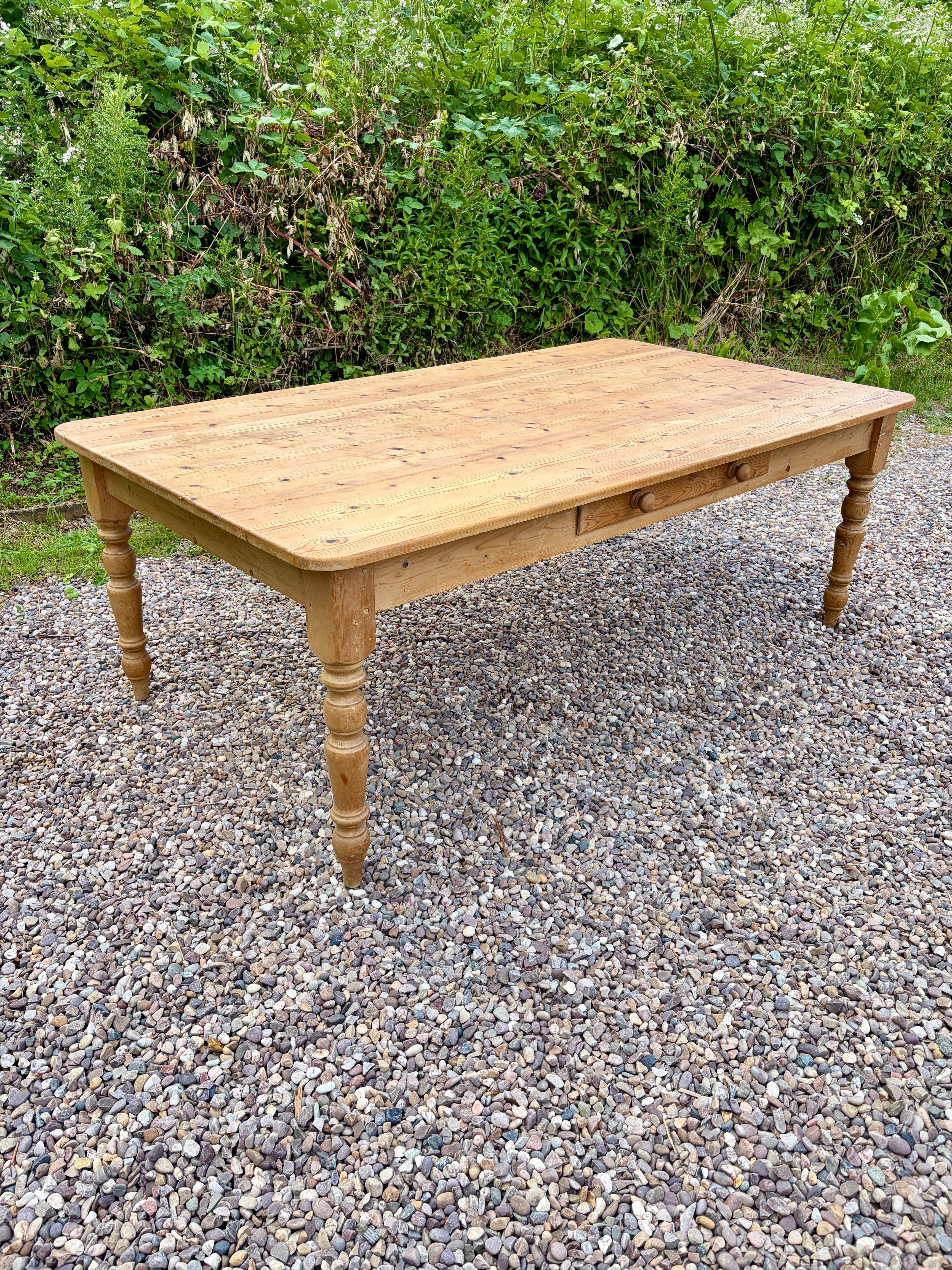 Wooden table on a gravel surface with greenery in the background