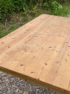 Wooden table top with natural grain and texture, outdoors on a gravel surface with greenery.