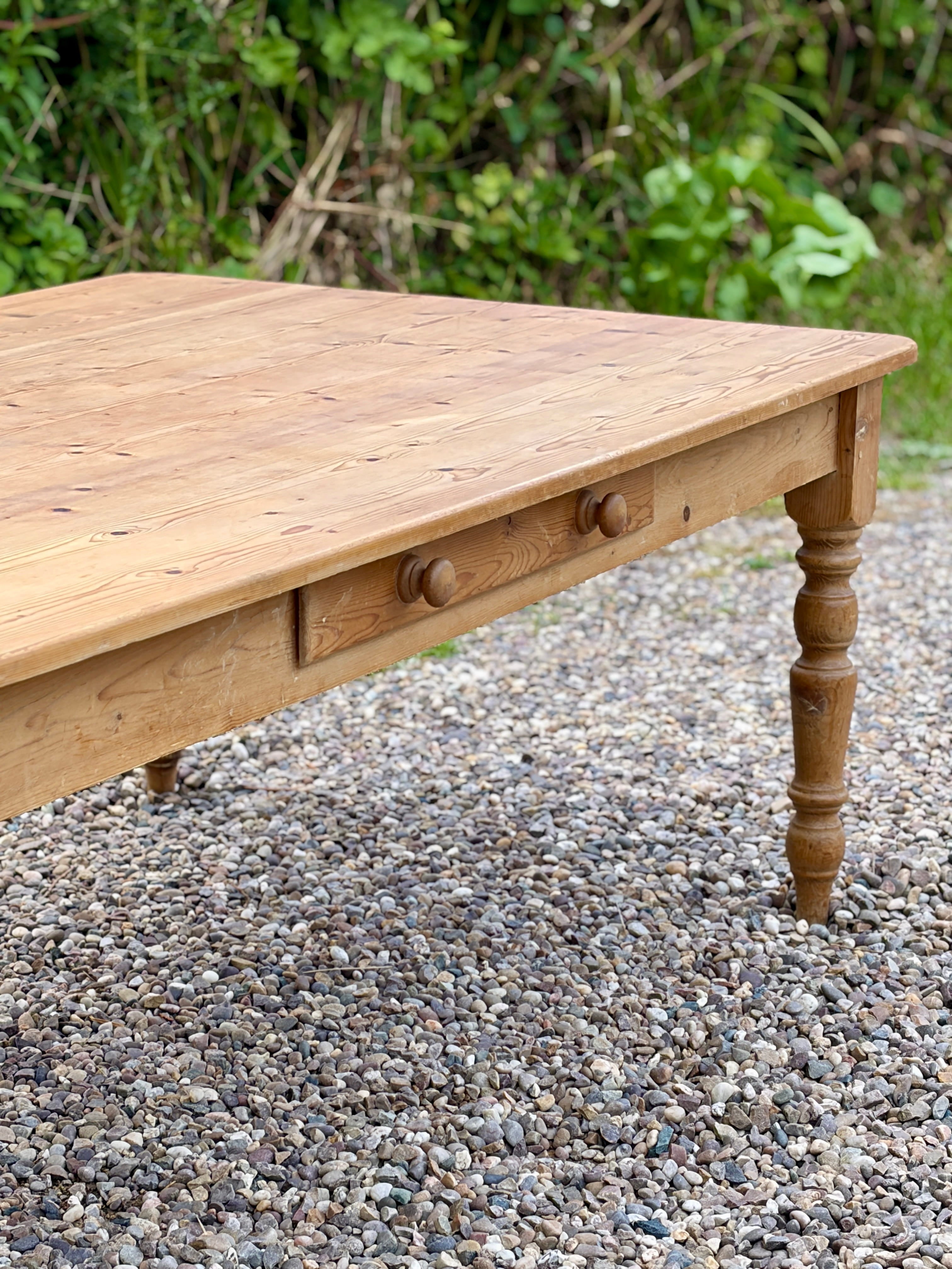 Wooden table with drawers on a gravel surface with greenery in the background
