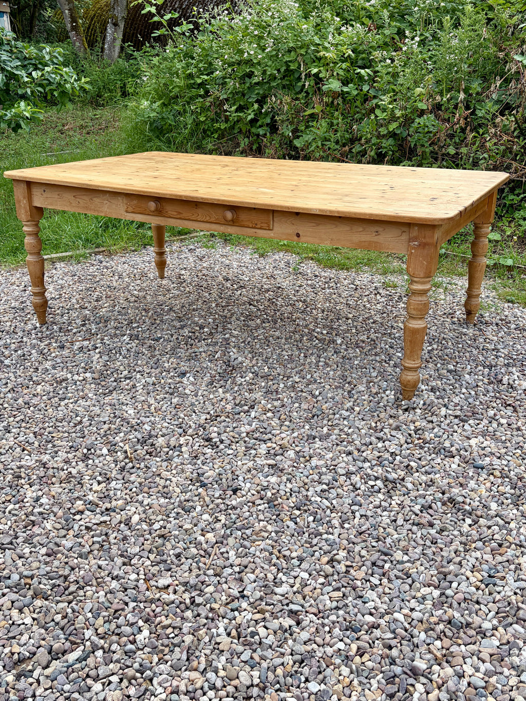 Wooden table on a gravel surface with greenery in the background
