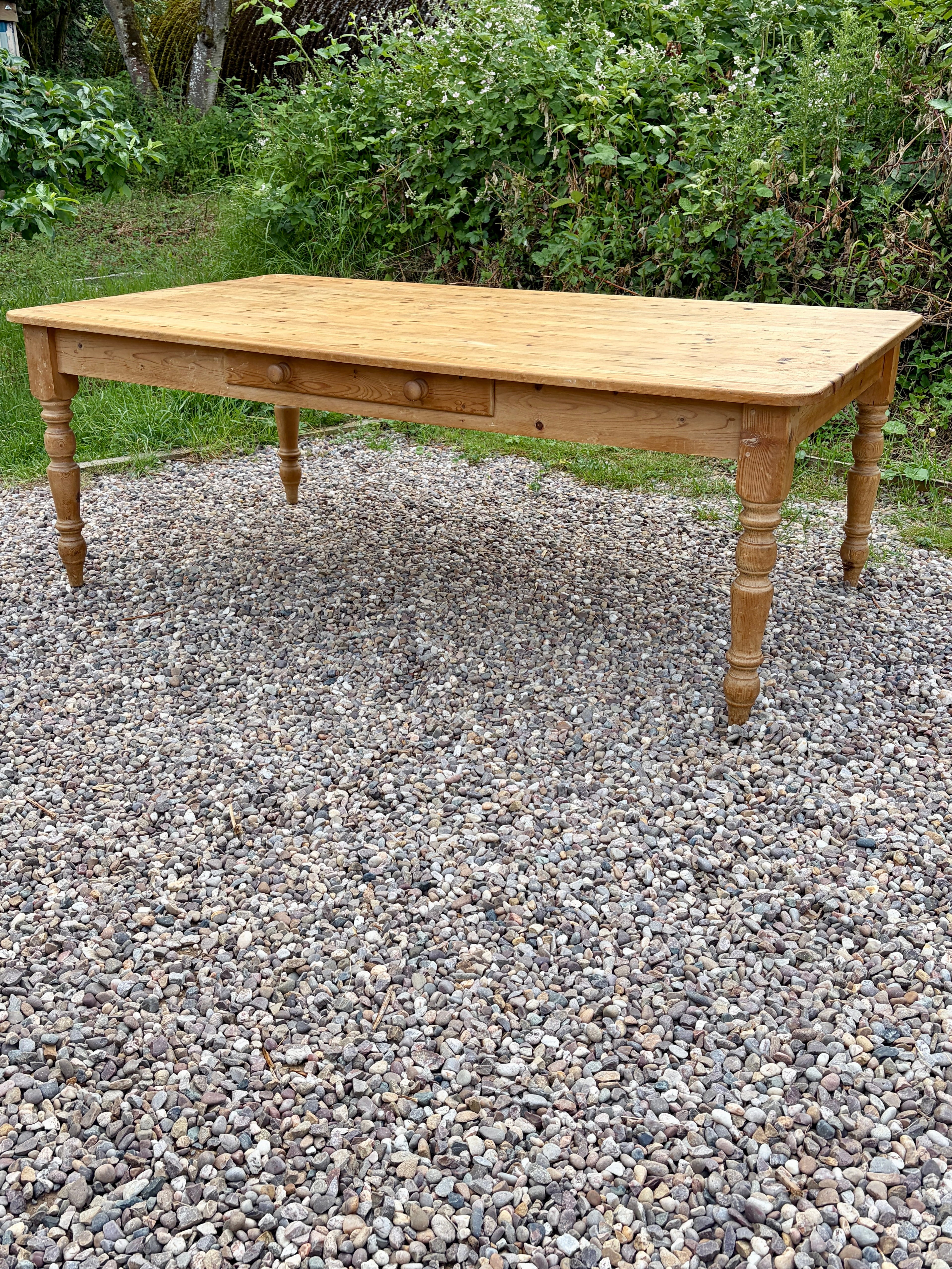 Wooden table on a gravel surface with greenery in the background