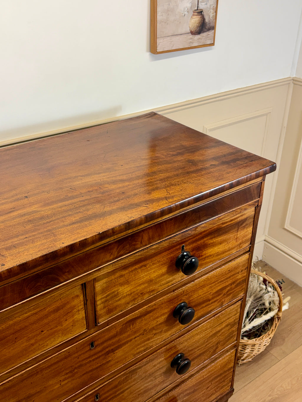 Wooden dresser with black knobs against a white wall with a framed picture.