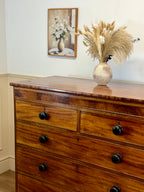 Wooden dresser with a vase of dried plants on top, framed artwork in the background