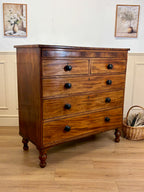 Wooden dresser with black knobs on a wooden floor with a white wall background