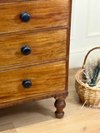 Wooden dresser with black knobs on a wooden floor next to a wicker basket.