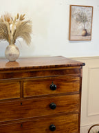 Wooden dresser with black knobs, vase of dried plants, and framed picture on a white wall.