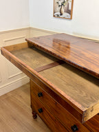 Wooden desk with an open drawer in a room with a painting on the wall.