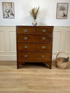 Wooden dresser with four drawers on a wooden floor, with two framed pictures on the wall.