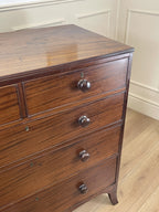 Wooden dresser with three drawers on a wooden floor against a white paneled wall.