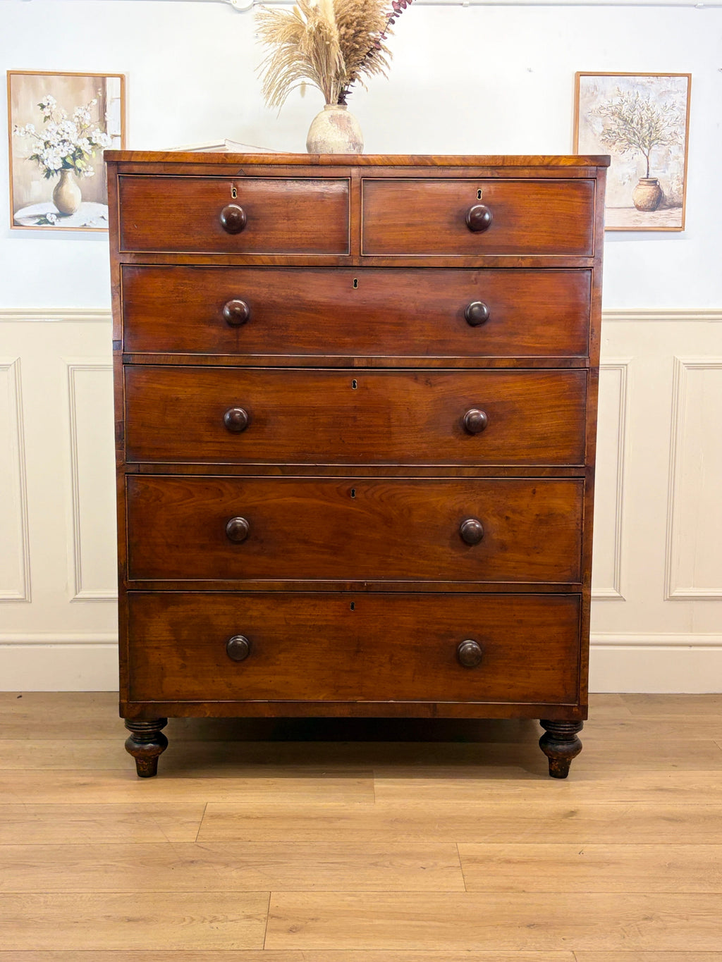 Wooden dresser with multiple drawers in a room with white walls and wooden floor.
