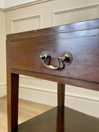 Wooden drawer with brass handle against a neutral wall.