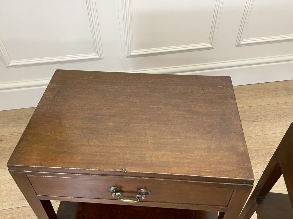 Wooden side table with a drawer against a white paneled wall.
