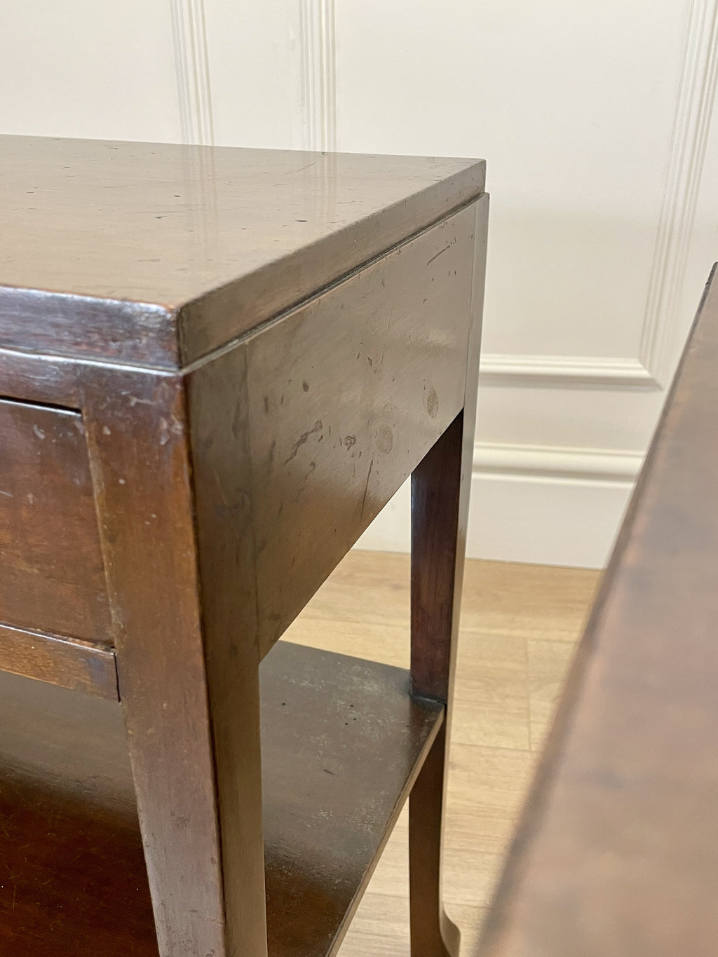 Wooden desk with wooden legs against a white paneled wall.
