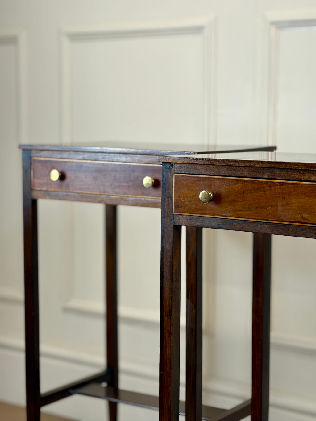 Wooden side table with two drawers against a white paneled wall
