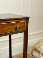 Wooden side table with a drawer and brass handle against a neutral wall.