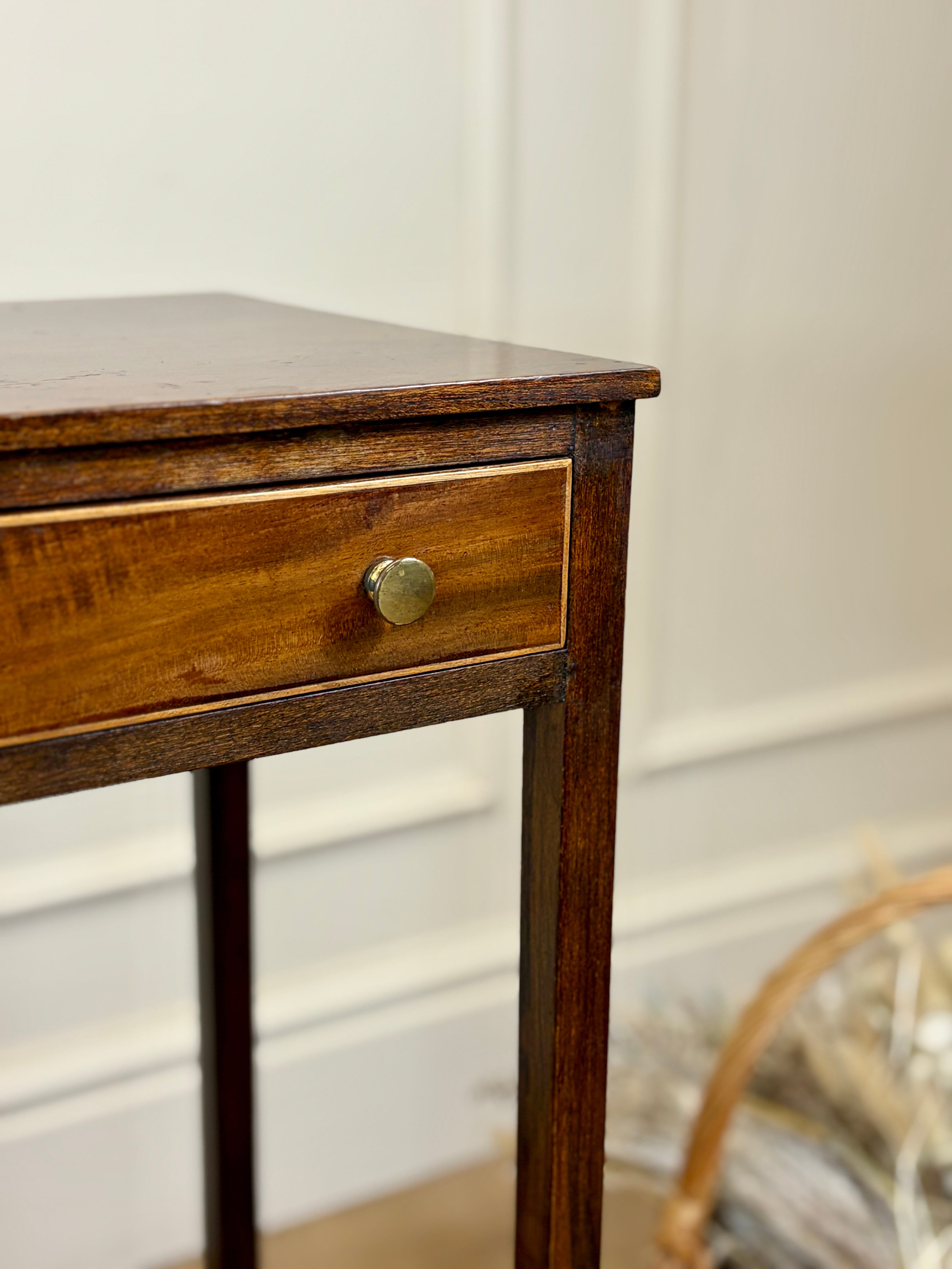 Wooden side table with a drawer and brass handle against a neutral wall.