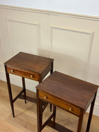 Two wooden side tables with drawers against a white paneled wall.