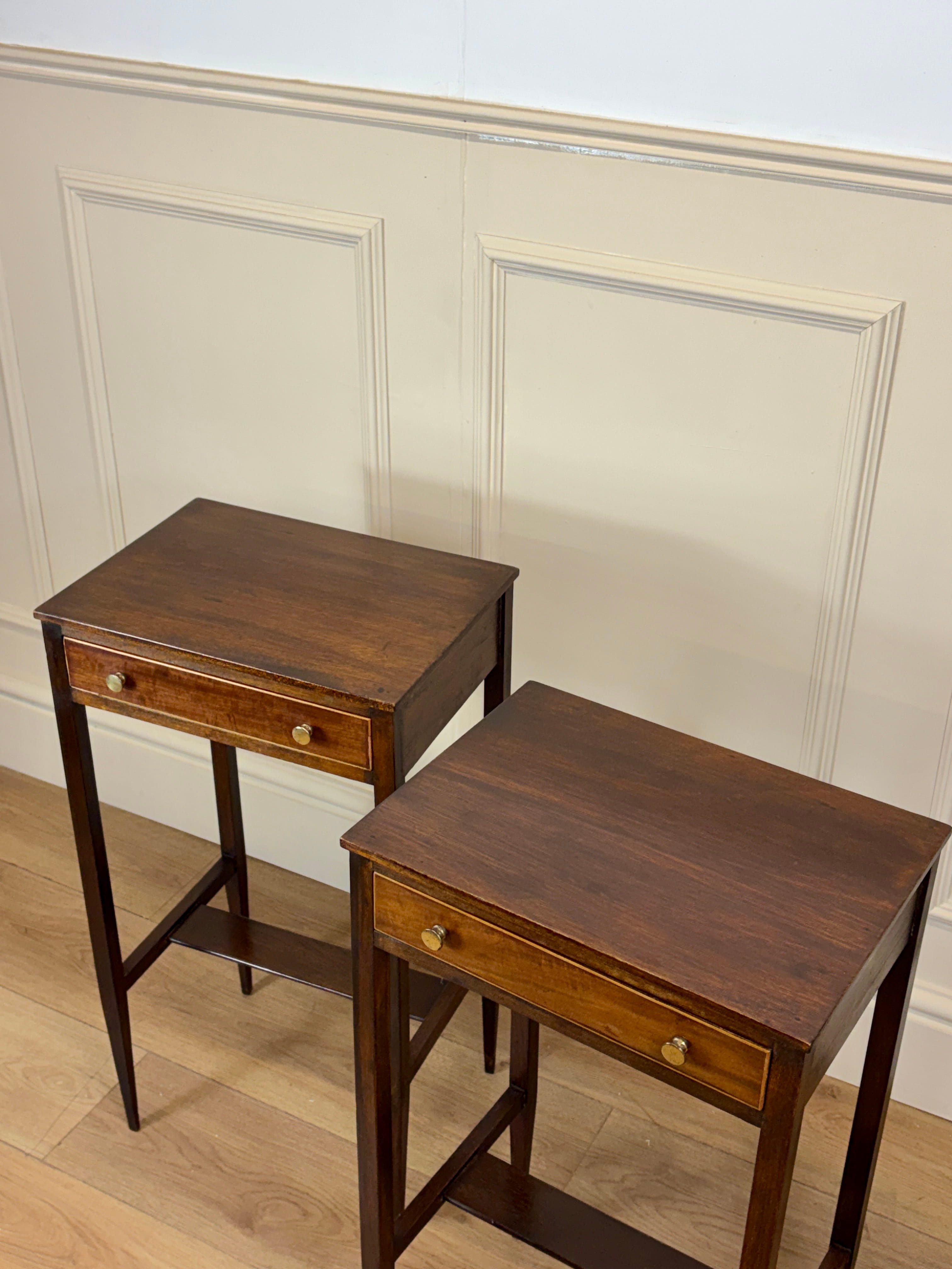 Two wooden side tables with drawers against a white paneled wall.