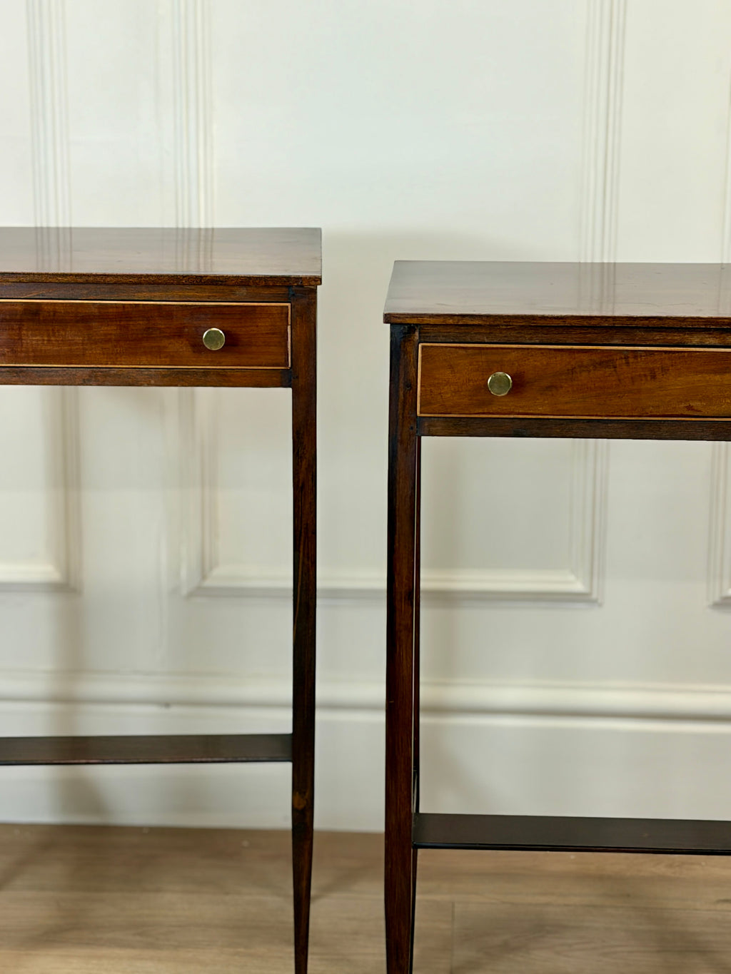 Two wooden side tables with glass tops against a white wall.