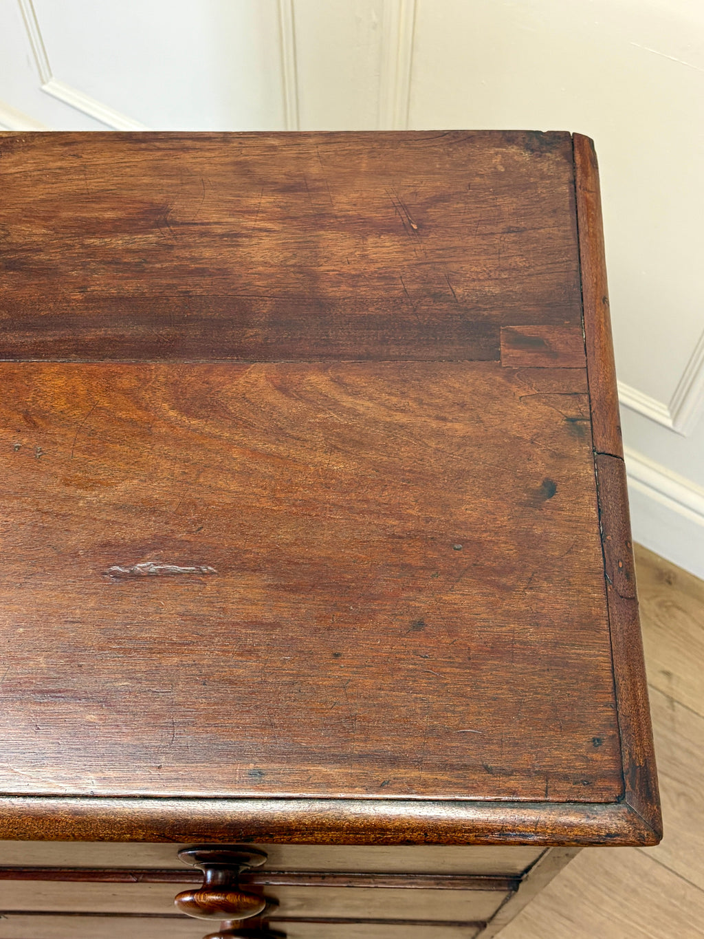 Wooden desk with a worn surface in a room with white walls and wooden floor.