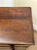 Wooden desk with a worn surface in a room with white walls and wooden floor.