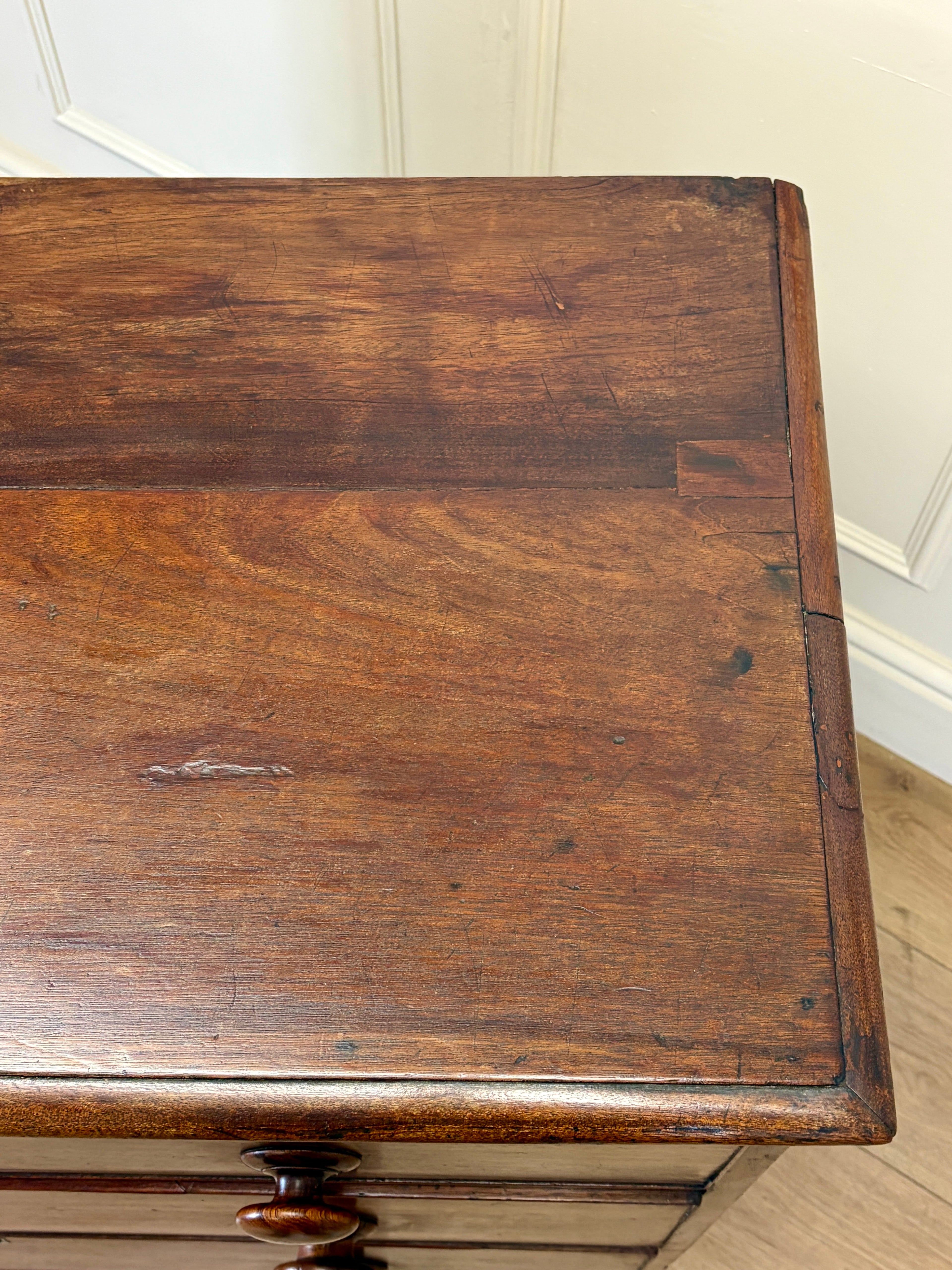 Wooden desk with a worn surface in a room with white walls and wooden floor.