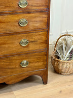Wooden dresser with brass handles next to a wicker basket on a wooden floor.