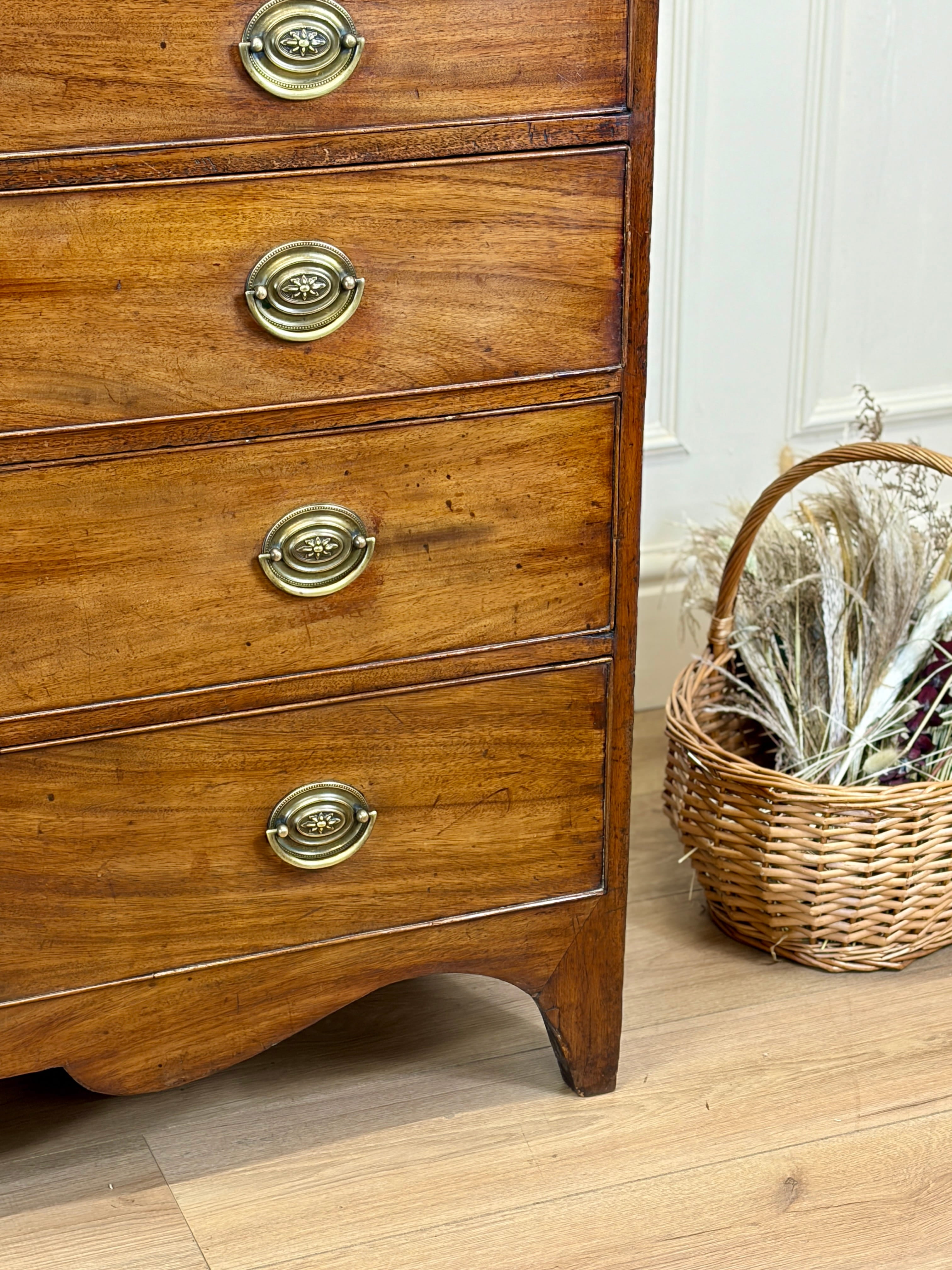 Wooden dresser with brass handles next to a wicker basket on a wooden floor.