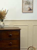 Wooden dresser with decorative items against a wall with paneling and a framed picture.