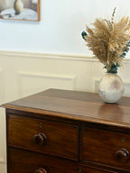 Wooden dresser with a vase of dried pampas grass on top, against a light wall.