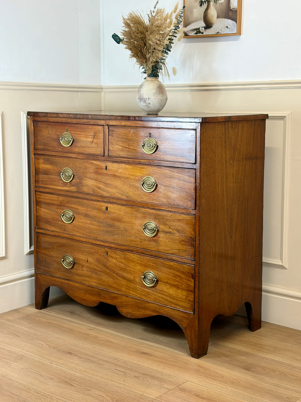Wooden dresser with brass handles in a room with a mirror and decorative vase.