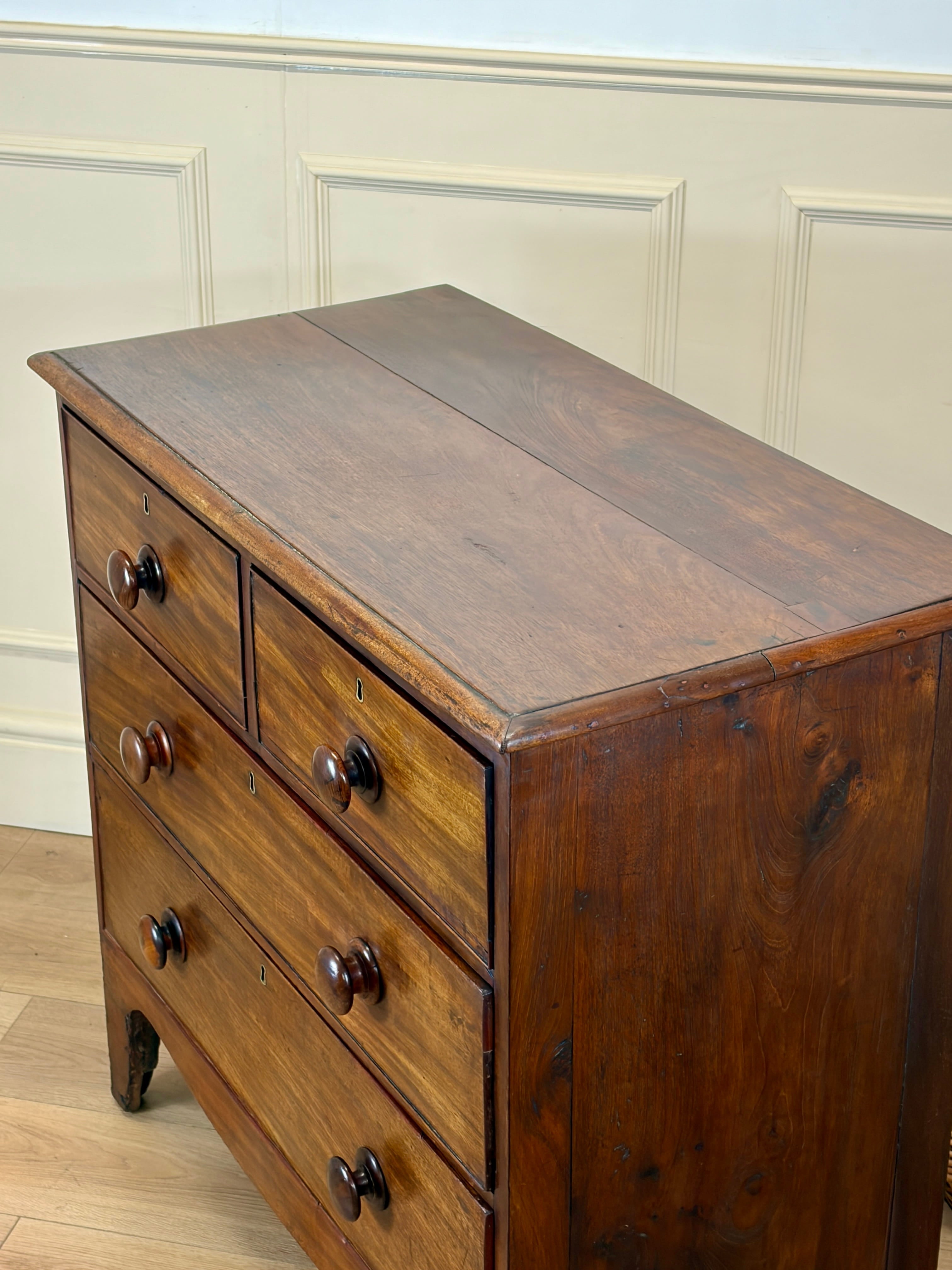 Wooden dresser with four drawers against a white paneled wall.