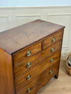Wooden dresser with brass handles against a white paneled wall.