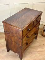 Wooden dresser with four drawers on a wooden floor against a white paneled wall.