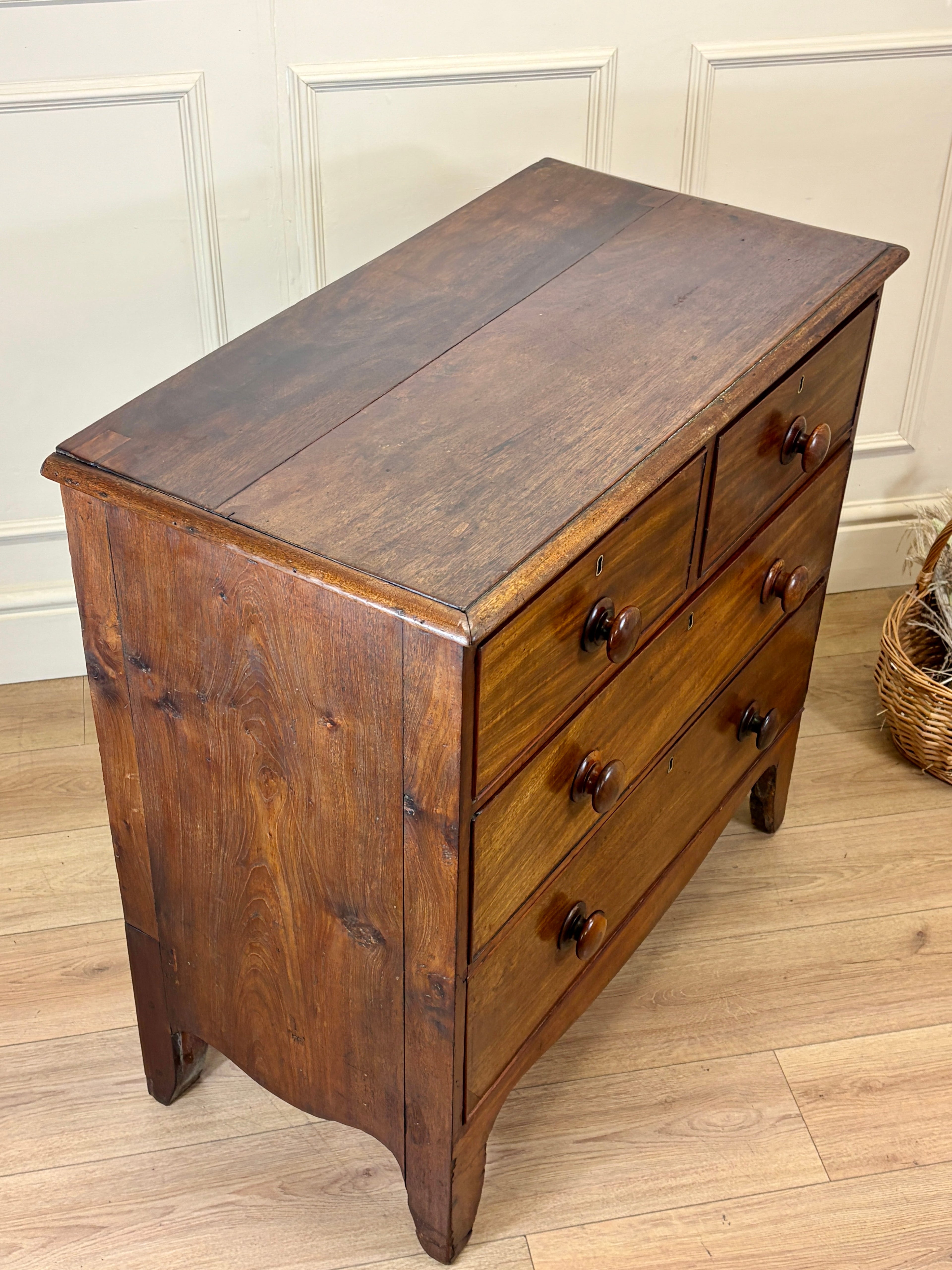 Wooden dresser with four drawers on a wooden floor against a white paneled wall.