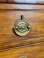 Close-up of a wooden drawer with a brass handle featuring a decorative design.