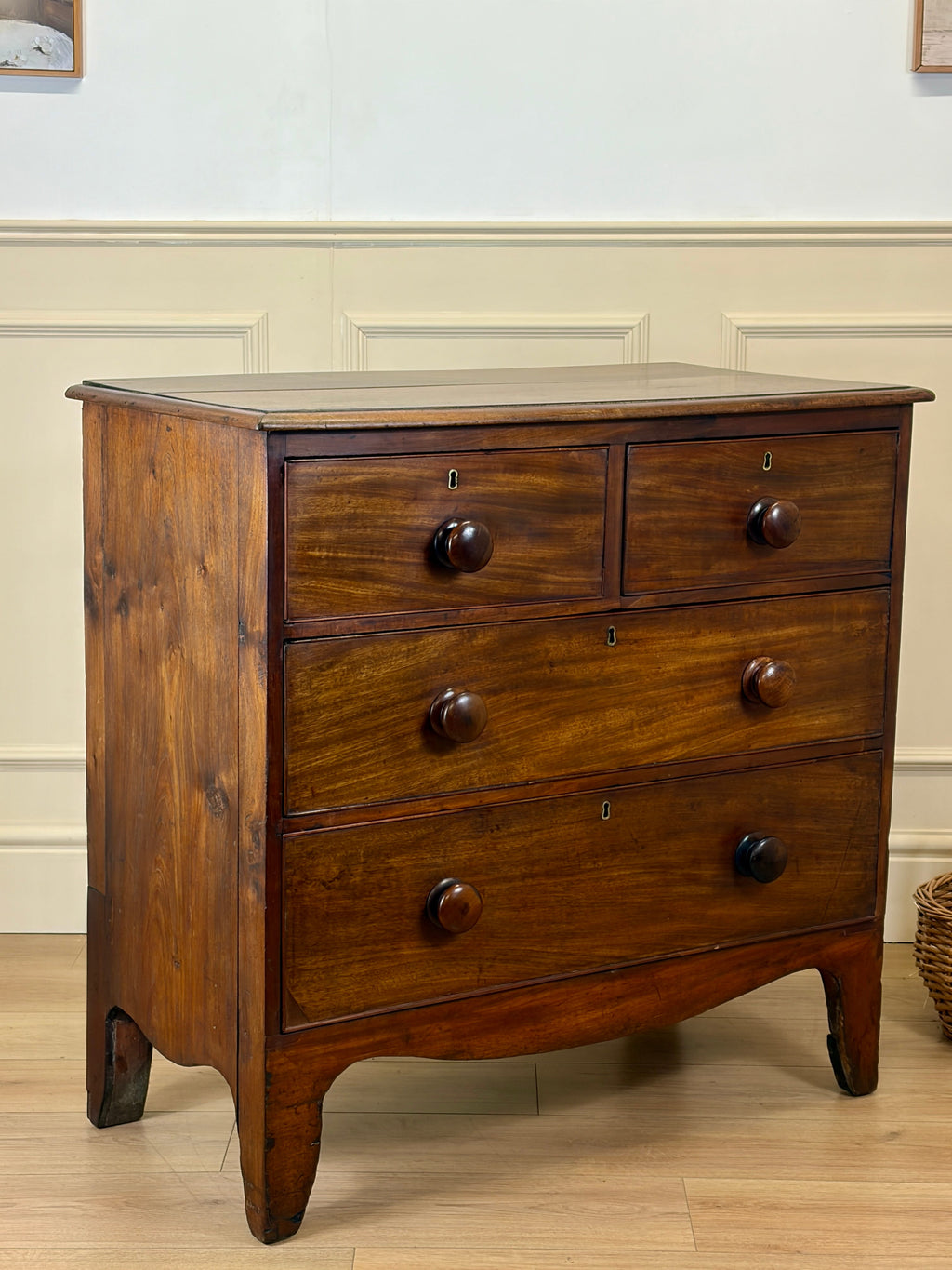 Wooden dresser with four drawers on a wooden floor against a white wall.