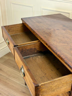 Wooden desk with open drawer against a white paneled wall.