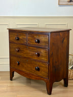 Wooden dresser with four drawers on a wooden floor against a light blue wall.