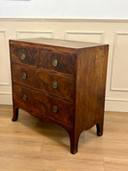 Wooden dresser with four drawers on a wooden floor against a white wall.
