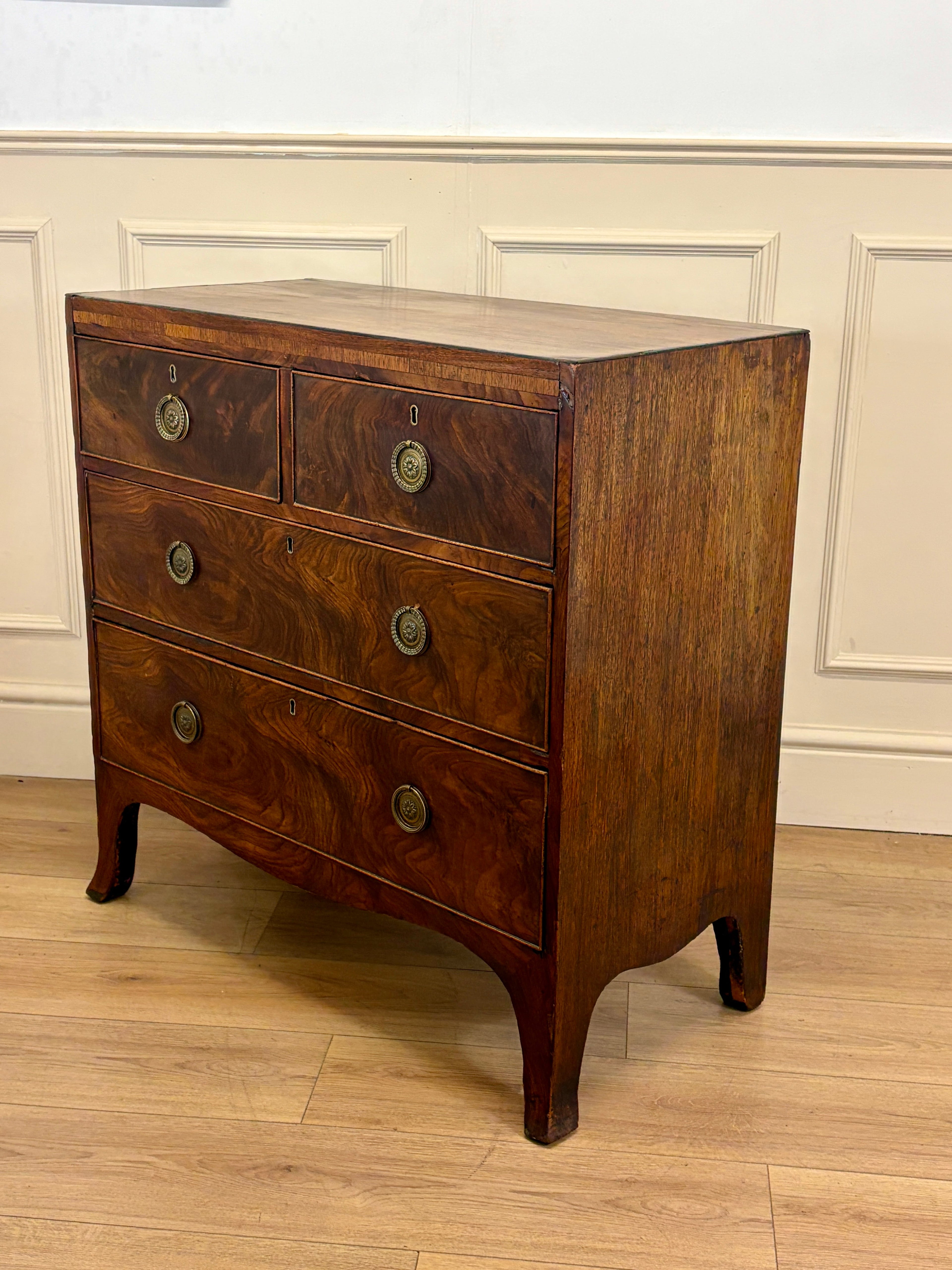 Wooden dresser with four drawers on a wooden floor against a white wall.