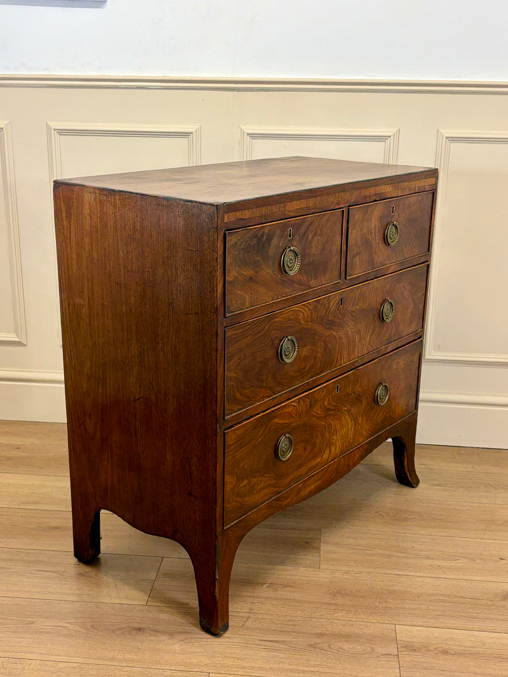Wooden dresser with four drawers against a white paneled wall.