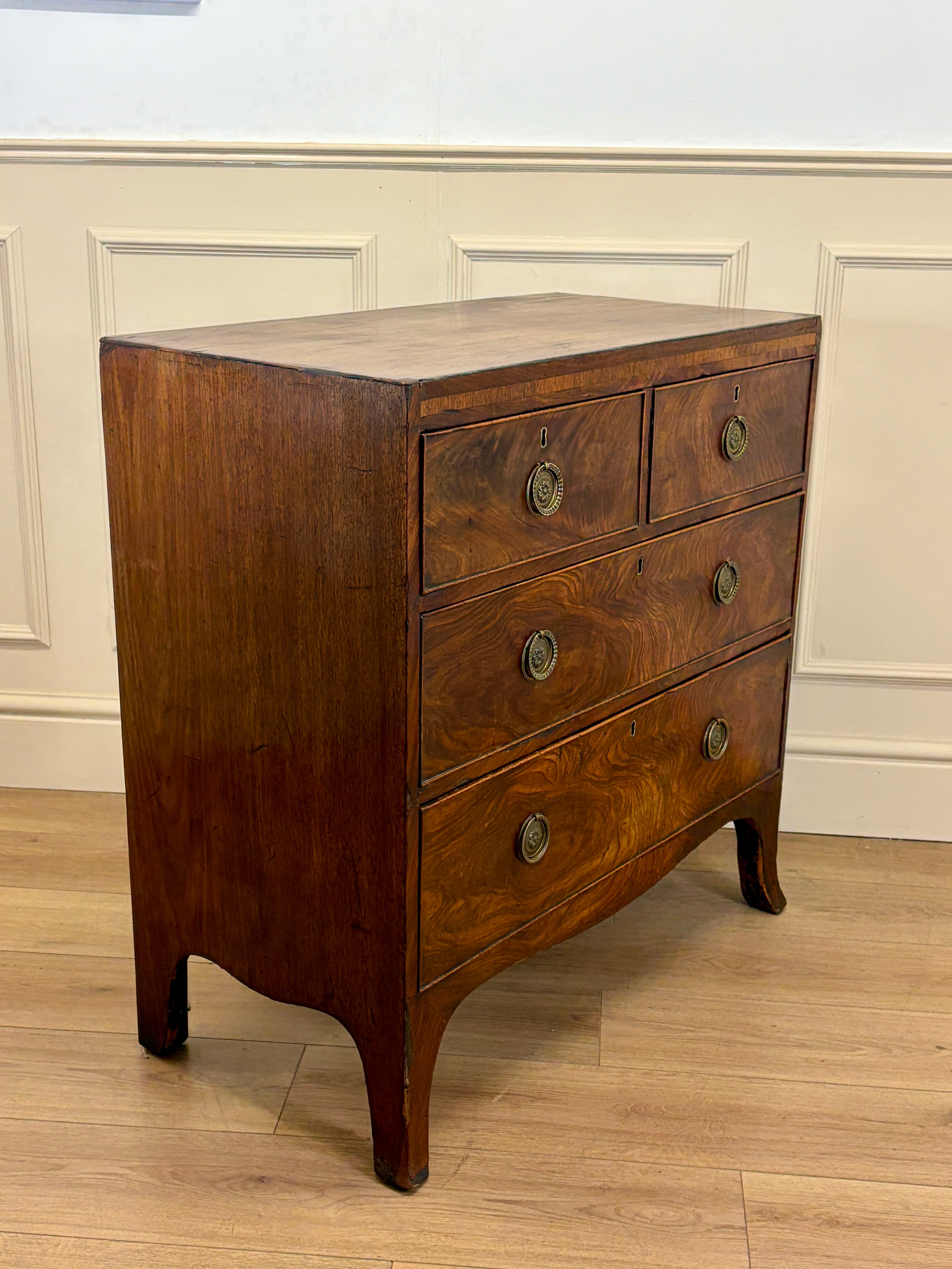 Wooden dresser with four drawers against a white paneled wall.