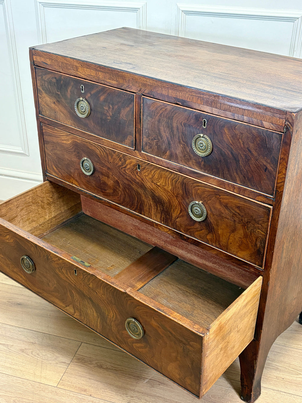 Wooden dresser with drawers and brass handles on a light wooden floor.
